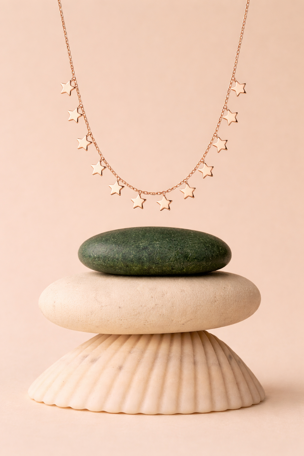 Rose gold necklace with star pendants on a stone and shell display against a beige background