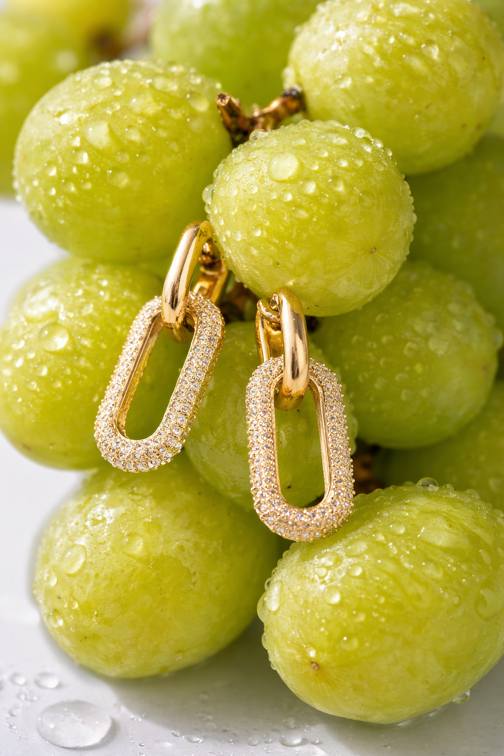 Valdor Lioré gold oval link earrings with pavé stones displayed on fresh green grapes with water droplets, luxury jewelry styling